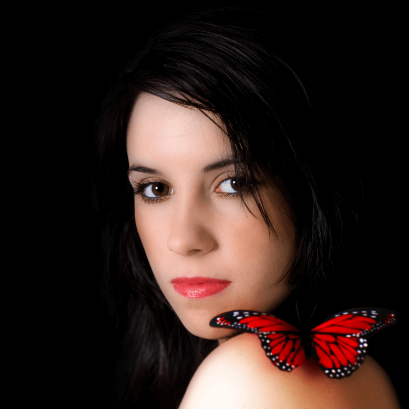 Žena s tmavými vlasy a červeným motýlem na rameni, vyzařující elegantní styl a krásu.