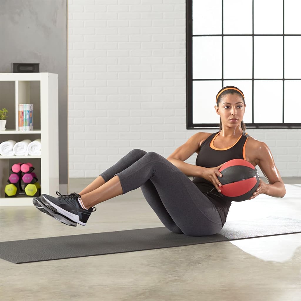 Žena cvičící s Ahoj Krása CoreBalance medicinbalem na podložce v moderním fitness prostředí.